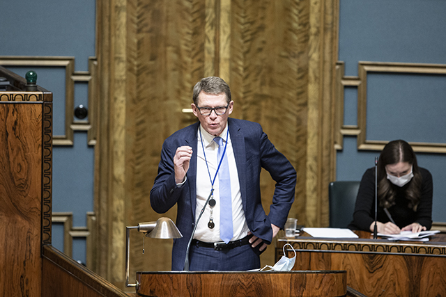 Valtiovarainministeri Matti Vanhanen puhuu seisten täysistuntosalin puhujakorokkeella. Taustalla istuu pääministeri Sanna Marin.