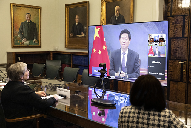 Puhemies Vehviläinen istuu pöydän vieressä ja katselee isoa näyttöä, jolla näkyy Kiinan kansankongressin puhemies.