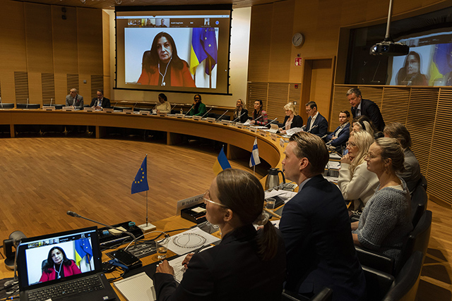 Suuren valiokunnan jäseniä kokoushuoneessa ja Ukrainan parlamentin jäsen seinänäytöllä